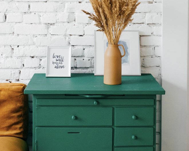 green chest of drawers with decorative plants and frames on it